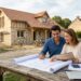 couple examinant des documents de financement devant une maison neuve en construction
