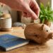 Main déposant une pièce d'un euro dans une tirelire en bois