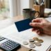 Main tenant une carte bancaire près d'un relevé de compte et d'une calculatrice